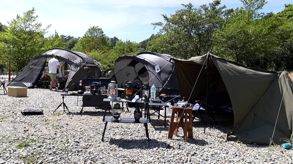 晴天のビッグオートサイト。複数のテントとランタン、砂利敷きの広い設営スペース