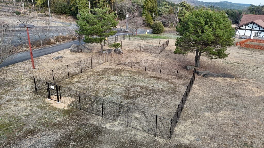 ドッグランエリアの俯瞰。複数のフェンス区画と道路、周辺の樹木や建物